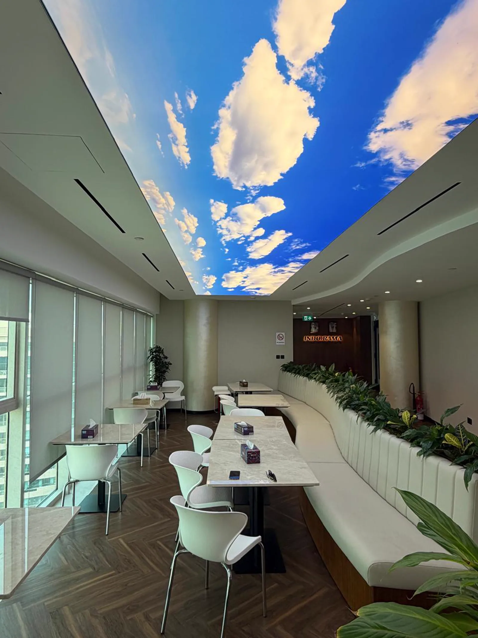 Staff breakout area with illuminated sky-print stretch ceiling, curved banquette seating and planters