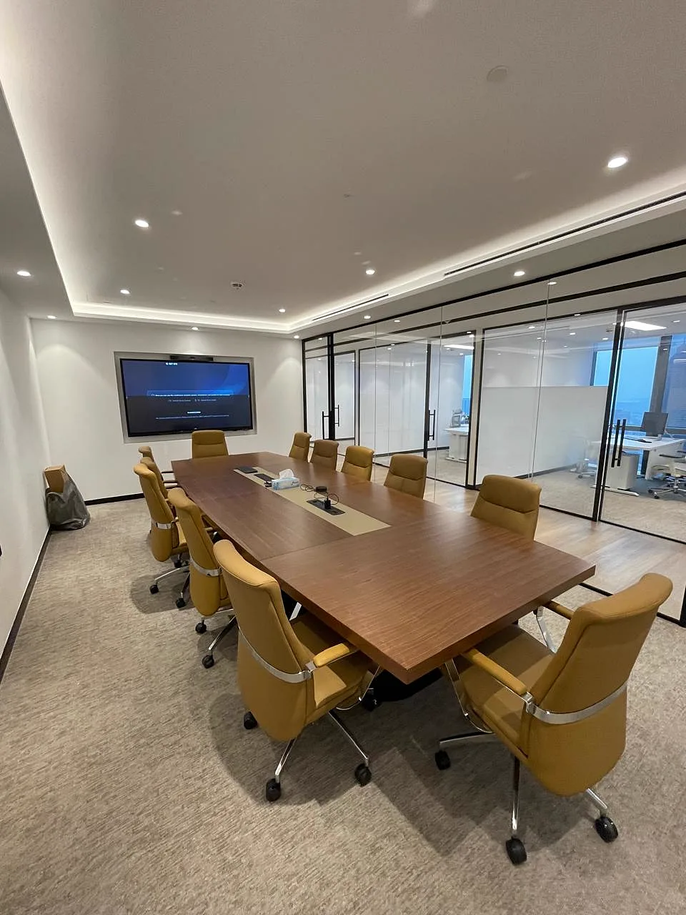 Boardroom with walnut conference table, tan leather chairs, wall-mounted display and glass partition to the office floor