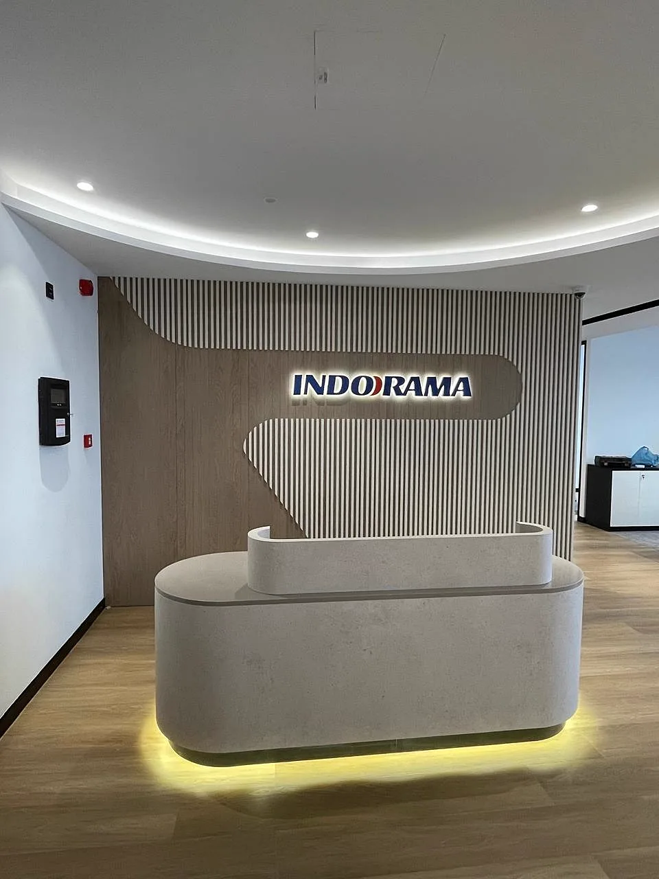 Backlit Indorama logo on a fluted timber feature wall above a curved stone reception counter with concealed lighting
