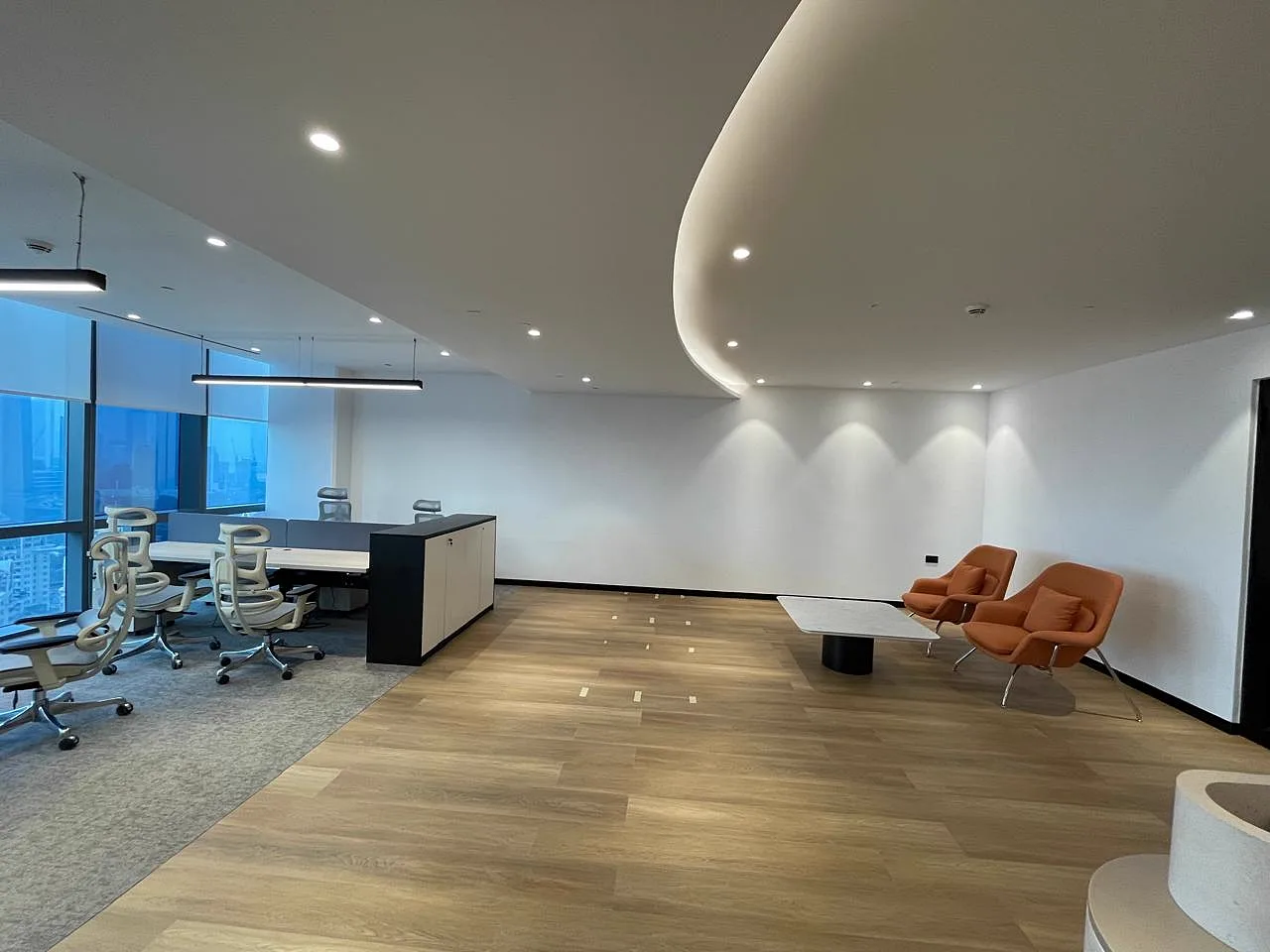Collaborative lounge with curved feature ceiling, wall washer lighting, orange armchairs and adjacent workstation bay