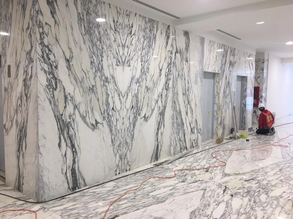 Book-matched marble wall cladding and polished marble flooring installed in a commercial lobby.