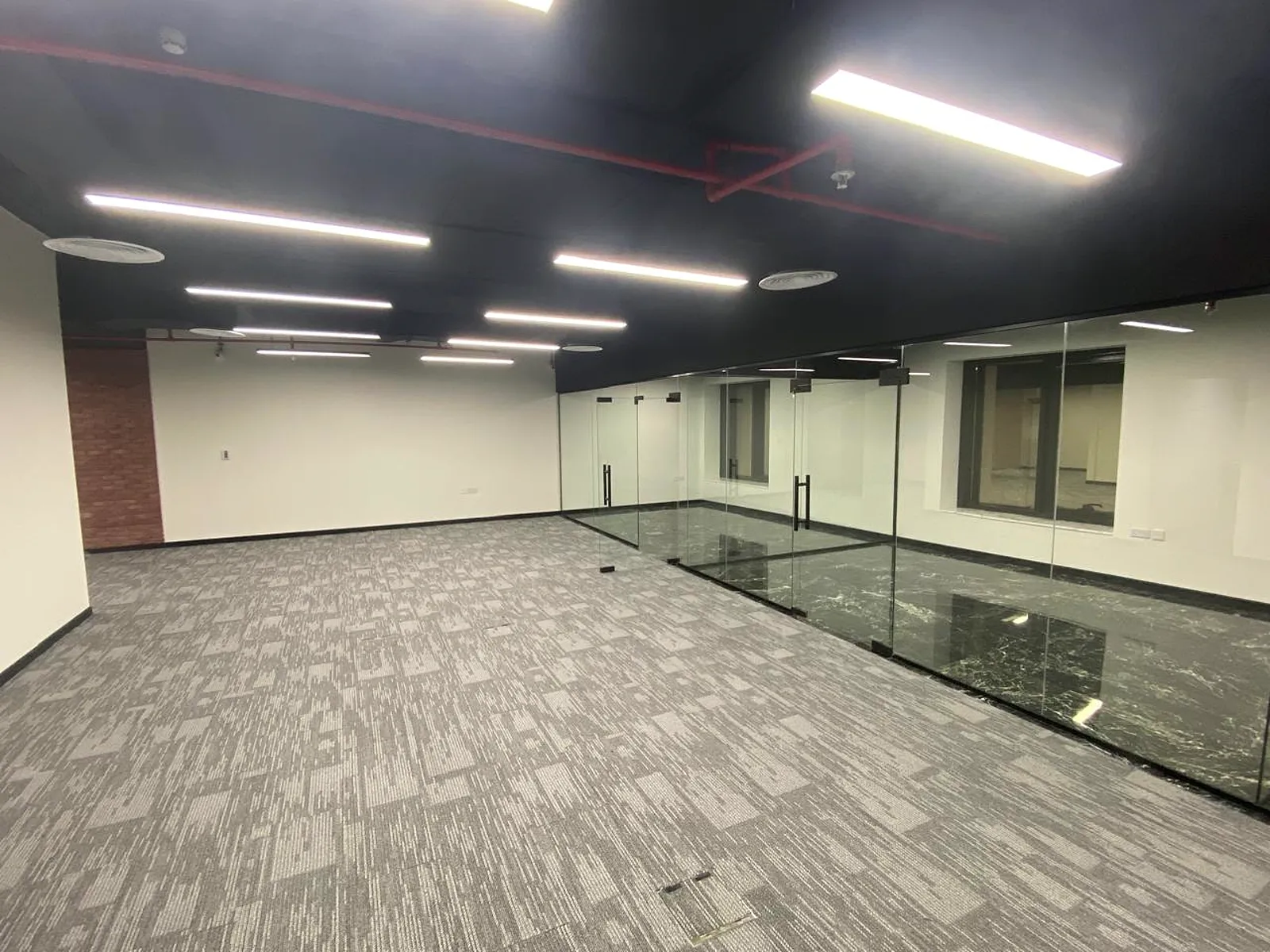 Enclosed glass offices with marble skirting, exposed black ceiling and linear LED lighting at MOODA Real Estate