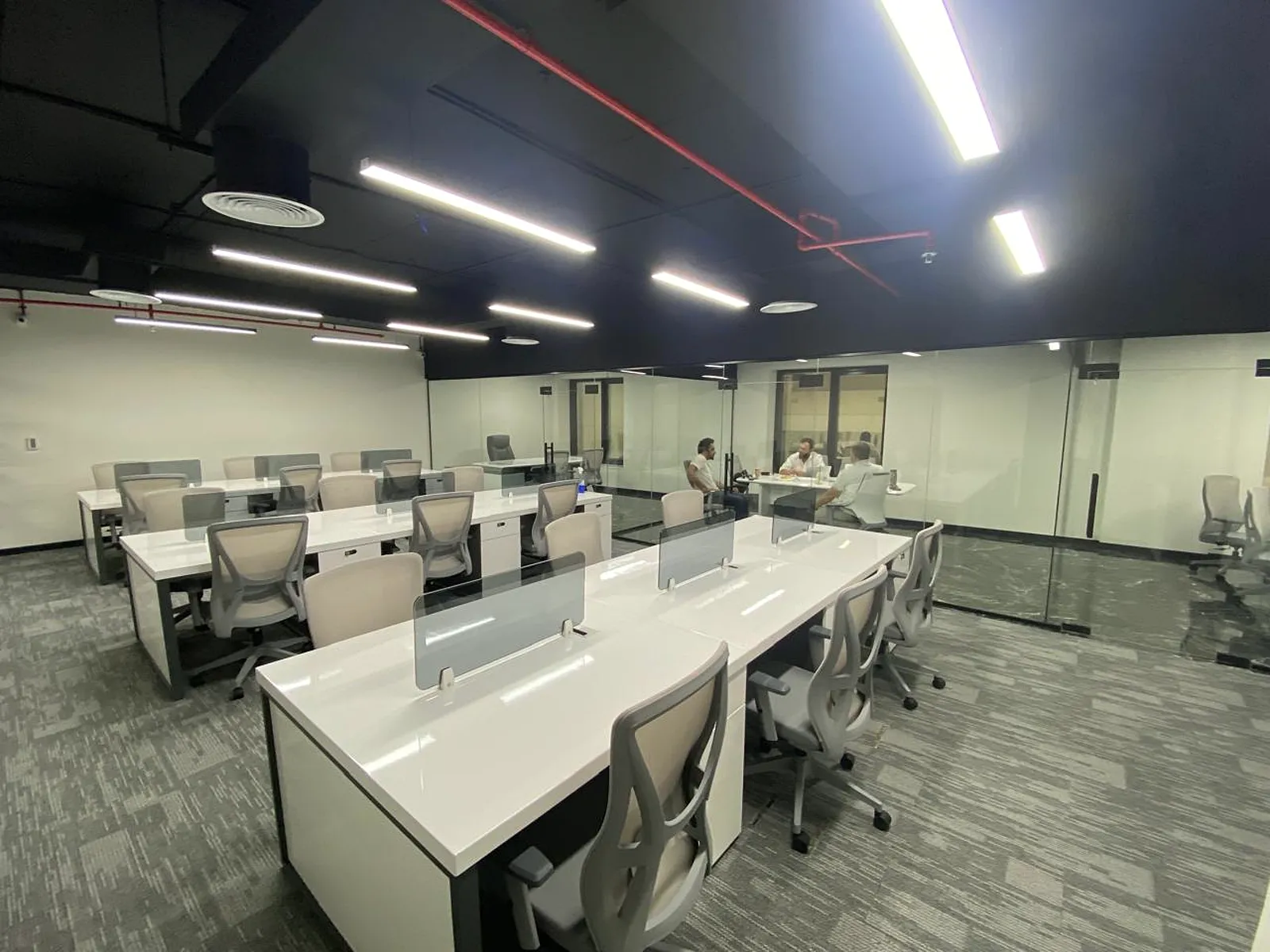 Open-plan office bays with grey carpet tiles and glass-partitioned discussion rooms in use