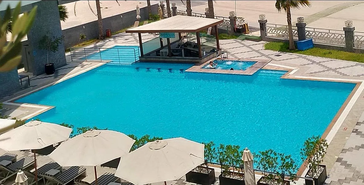 Completed swimming pool at Park Regis by Prince Hotel with tiled deck, shaded pool bar, jacuzzi and parasol seating area
