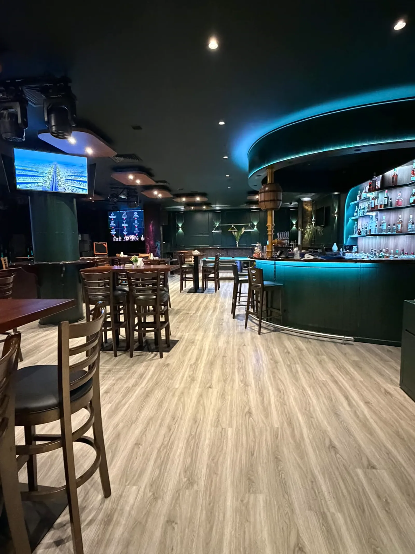Illuminated curved bar with backlit spirit shelving, brass column detail and timber-effect flooring at Retox Bar