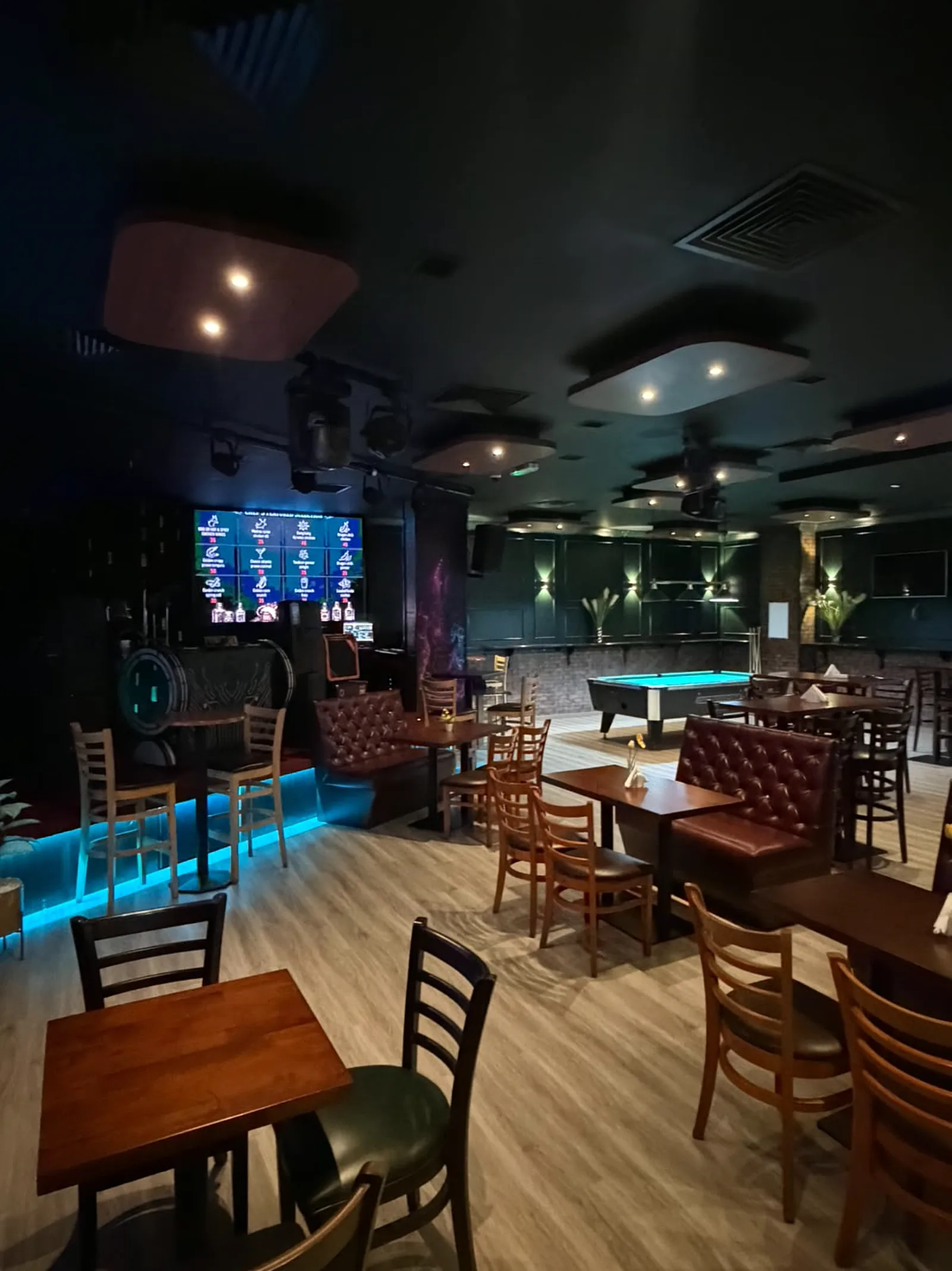 DJ booth and cocktail screen wall with blue LED plinth lighting beside pool table and lounge seating at Retox Bar